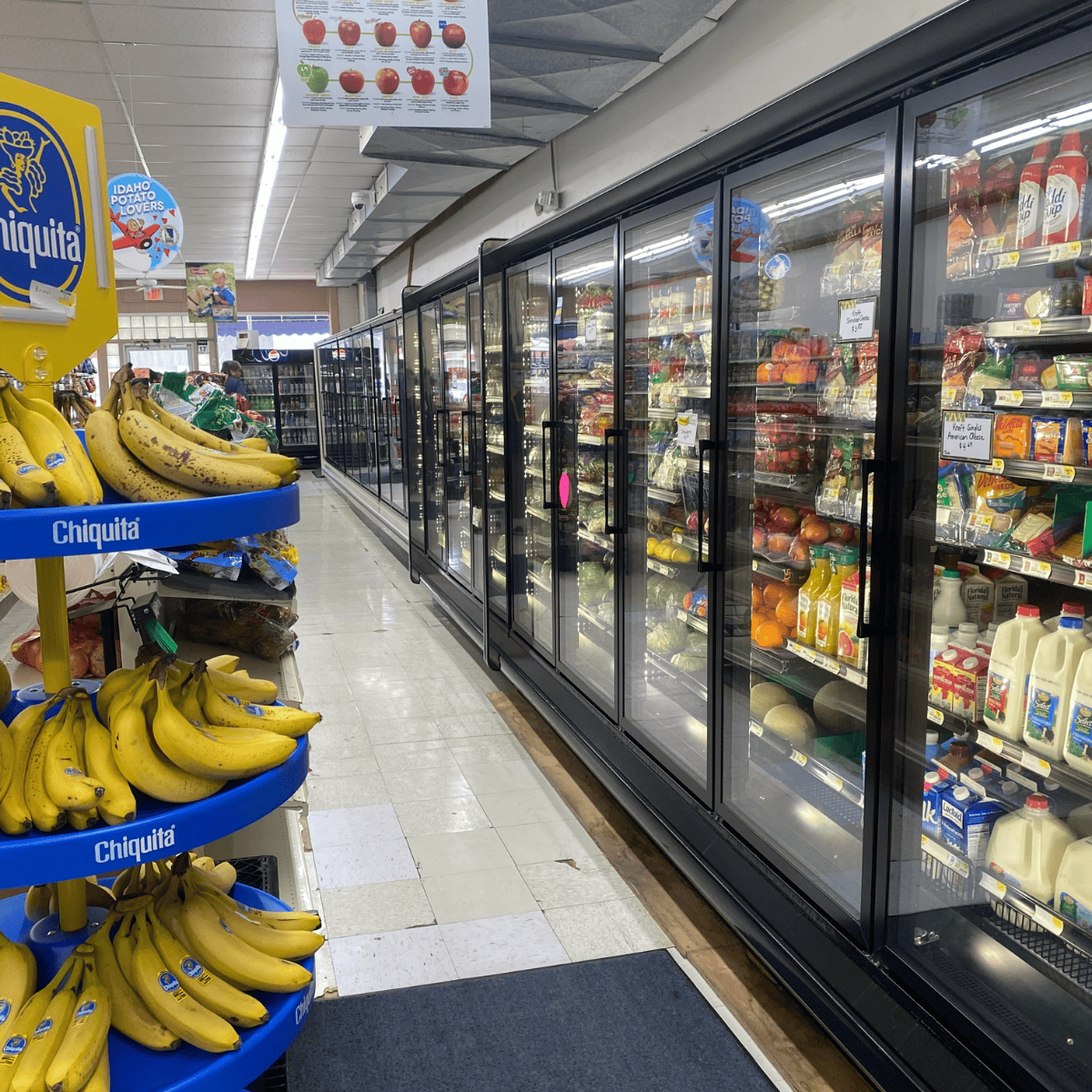 Grocery aisle at Greg's Market featuring bananas and a refrigerated section with milk, juice, and produce